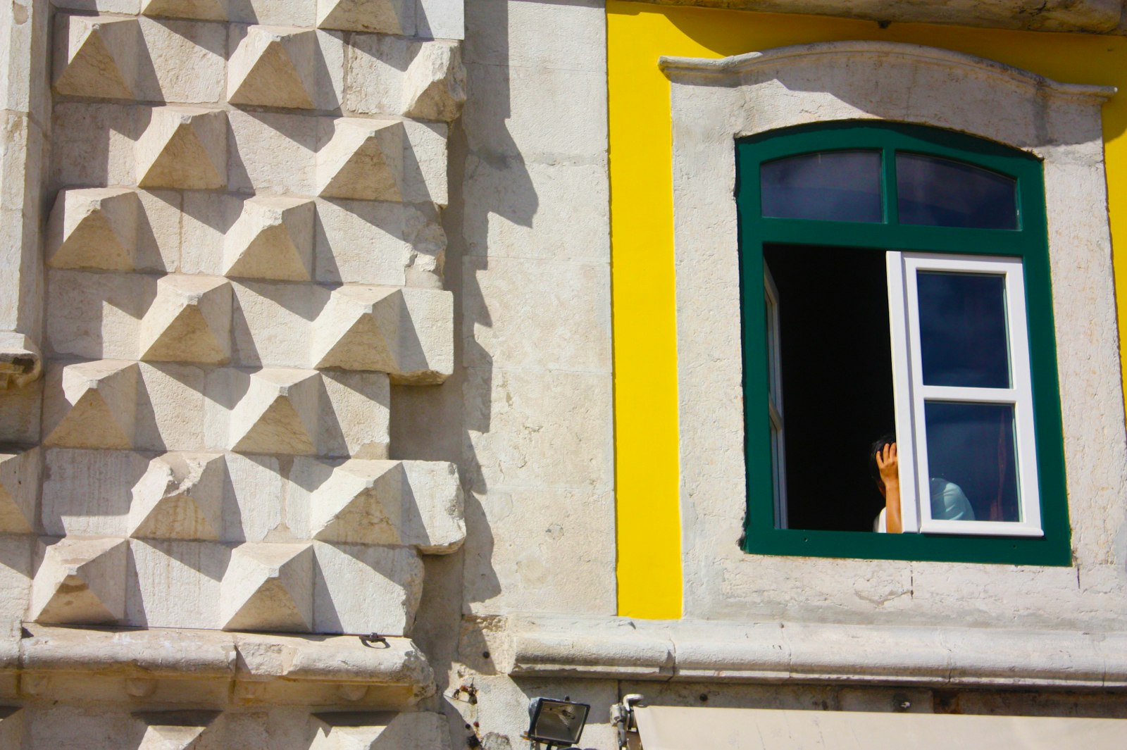 Blue wooden window frame on a yellow Lisbon facade in warm morning light